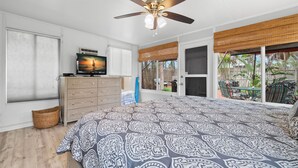 Un dormitorio con cama, ventilador de techo, cómoda, televisor y vistas al exterior.
