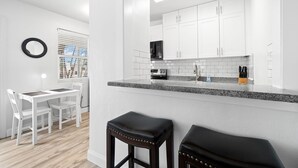 Una cocina moderna con armarios blancos, encimera de granito y microondas negro.