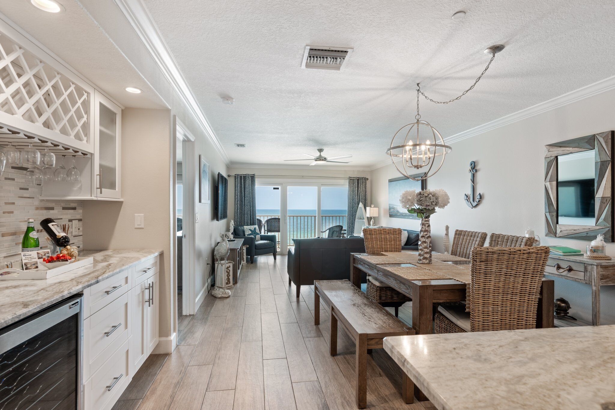A modern kitchen with white cabinetry, a marble countertop, and a dining area with wicker furniture and a chandelier.