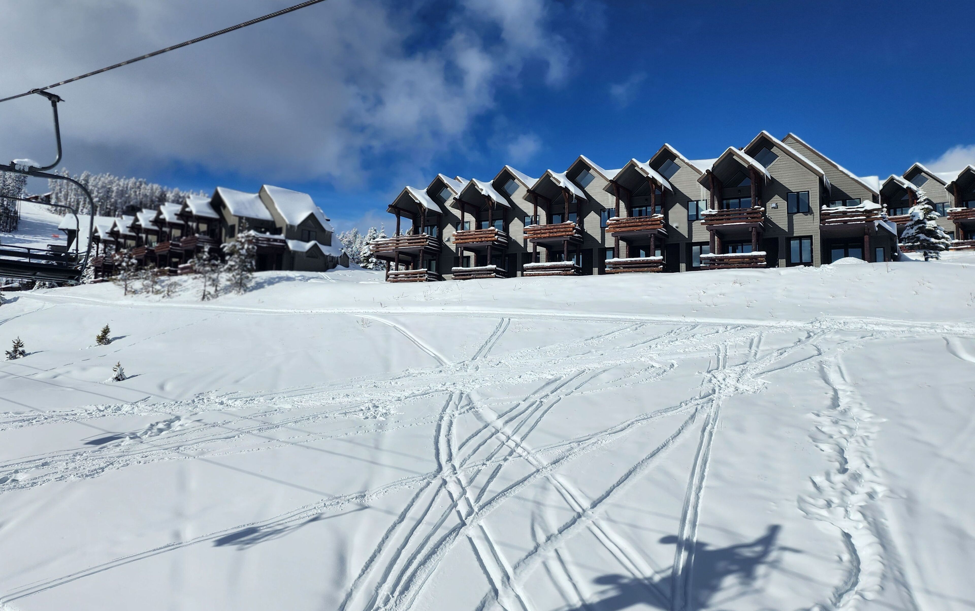 En rad av byggnader i chalet-stil med skidliftar synliga i bakgrunden.