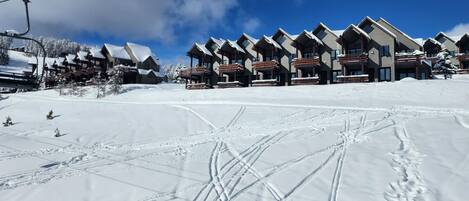 En rad av byggnader i chalet-stil med skidliftar synliga i bakgrunden.