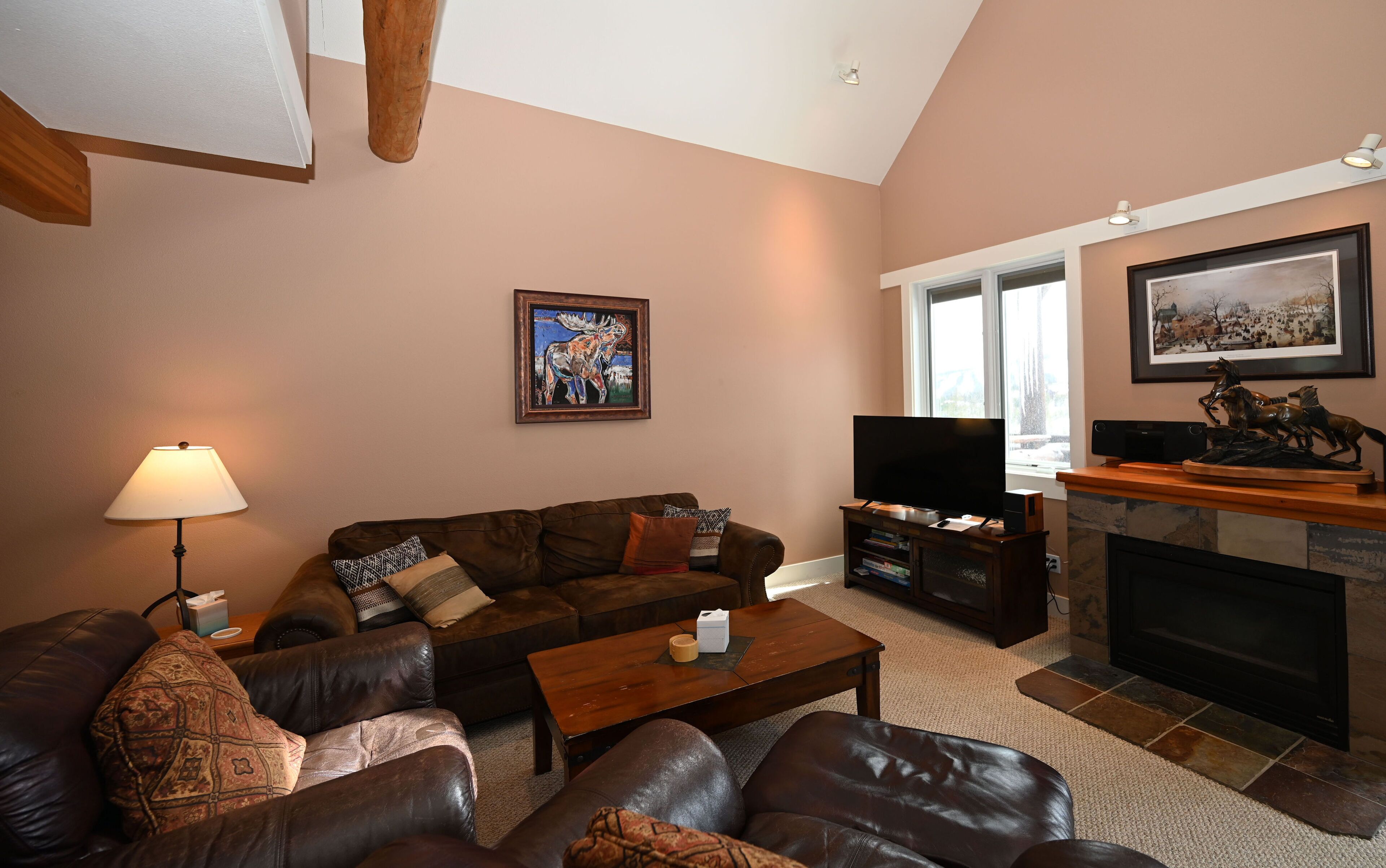 A living room with a brown leather sofa, a coffee table, a TV, a fireplace, and a painting on the wall.