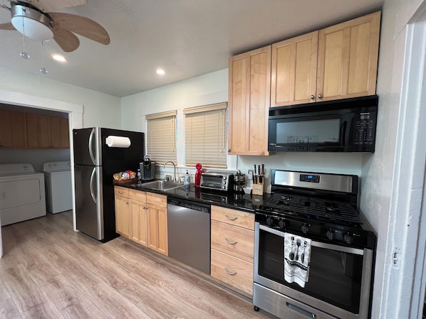 A modern kitchen with stainless steel appliances, wooden cabinets, and a black countertop. - Waterfront Historic Bungalow One• Ferry to SF (Vallejo)