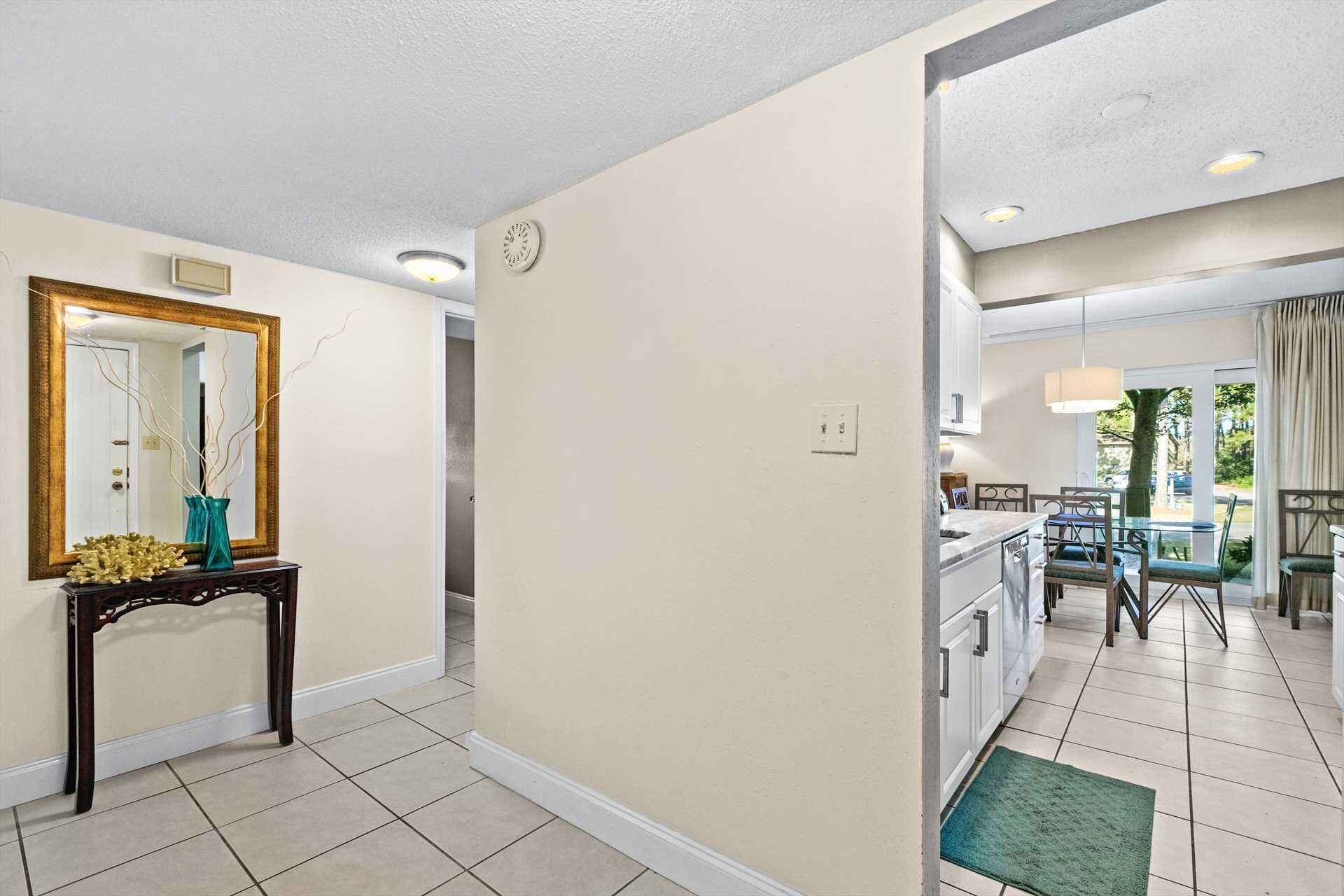 A hallway with a mirror, a vase, and a door leading to a dining area with a table and chairs.