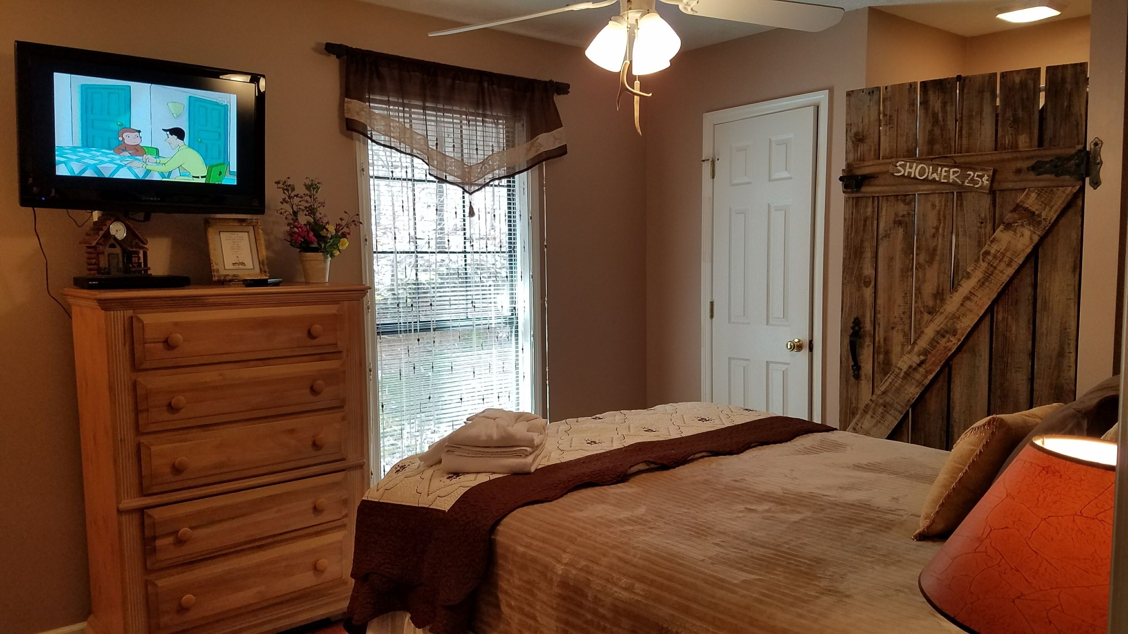 Une chambre à coucher avec un lit, une commode, une télévision et un panneau indiquant la présence d’une douche.