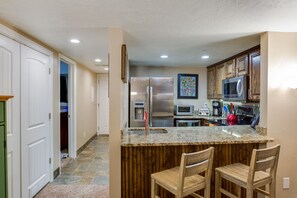 Una cocina con encimera de granito, electrodomésticos de acero inoxidable, armarios de madera y una zona de bar con dos sillas.