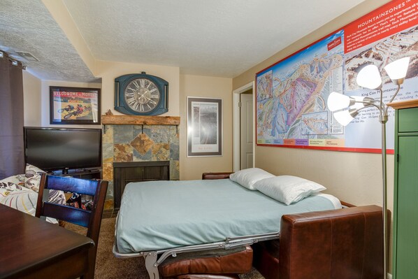 Una habitación de hotel con una cama, televisión, chimenea, un mapa en la pared y un cartel con un mapa.
