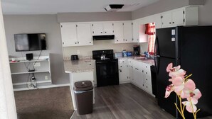 A modern kitchen with white cabinets, a black refrigerator, a stove, and a TV. - Private Upscale Condo in Myrtle w/ Ocean View Across from Boardwalk w/ Huge Deck (Myrtle Beach)