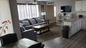 A modern living room with a sofa, coffee table, and a TV. There is a kitchen with white cabinets and a black refrigerator. - Private Upscale Condo in Myrtle w/ Ocean View Across from Boardwalk w/ Huge Deck (Myrtle Beach)
