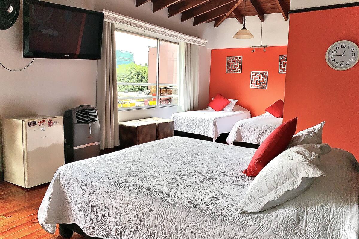 Habitación de hotel con dos camas, televisión, ventana con vistas y un reloj en la pared.