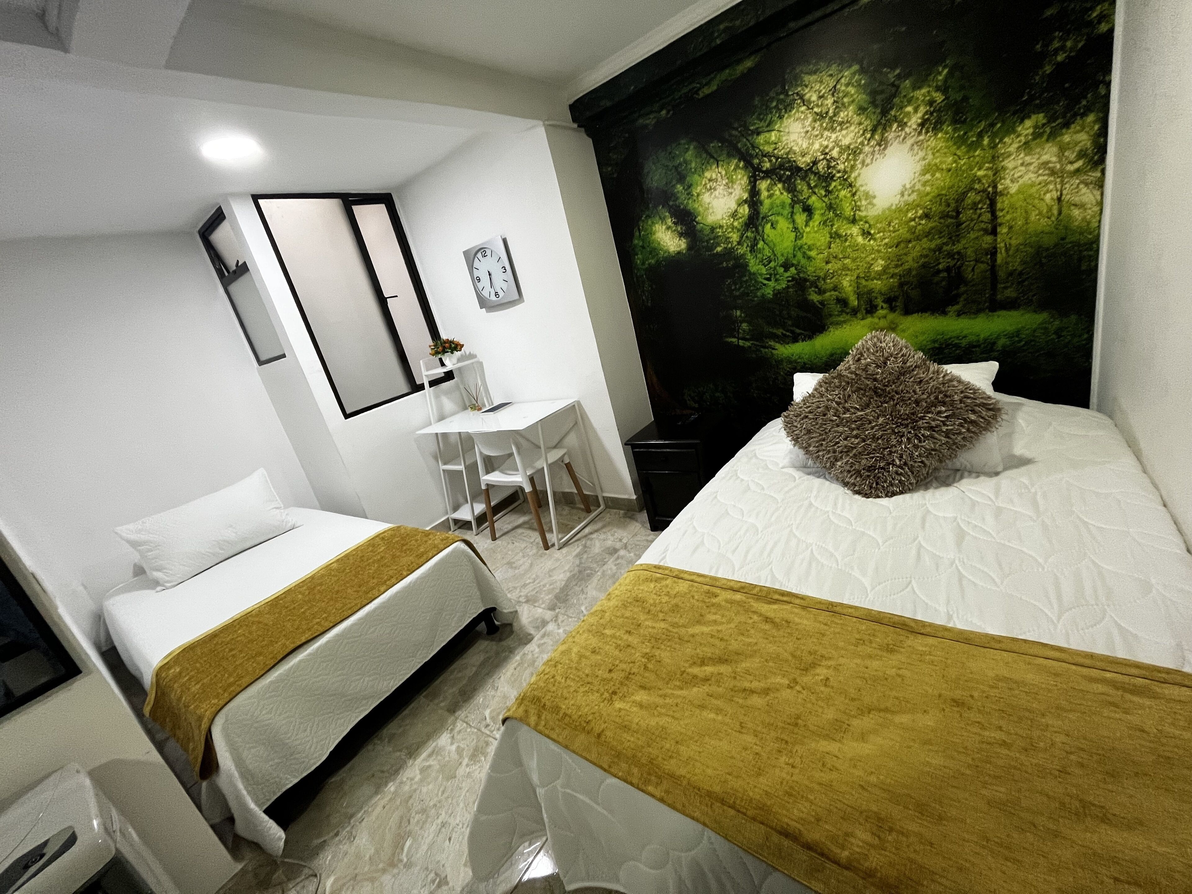 A hotel room with two beds, a desk, a chair, and a large forest mural on the wall.