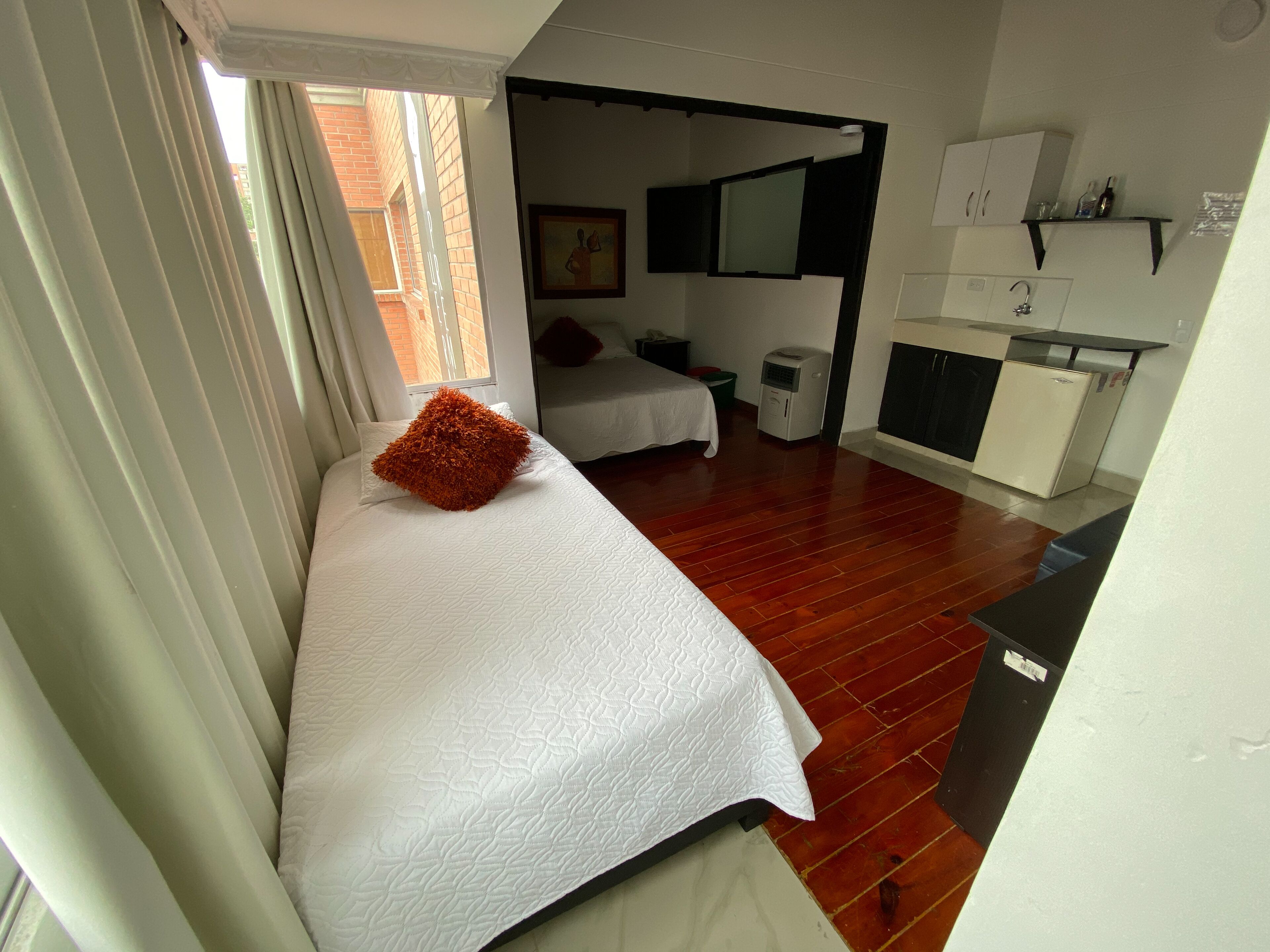 Ein Schlafzimmer mit Bett, kleinem Schreibtisch, Spiegel und einer Küchenzeile.
