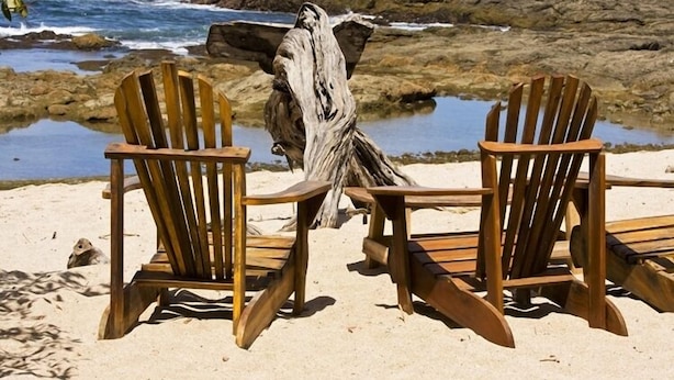 Dos sillones Adirondack de madera frente a una costa rocosa con una masa de agua.