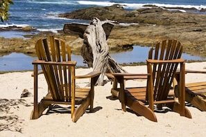 Two wooden Adirondack chairs facing a rocky shoreline with a body of water.