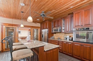 A kitchen with wooden cabinets, stainless steel appliances, a granite countertop, and a ceiling fan.