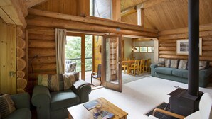 L’intérieur d’une cabane en rondins, avec un plafond en bois, un canapé, une table sur laquelle se trouvent un livre et une tasse, et une cheminée.