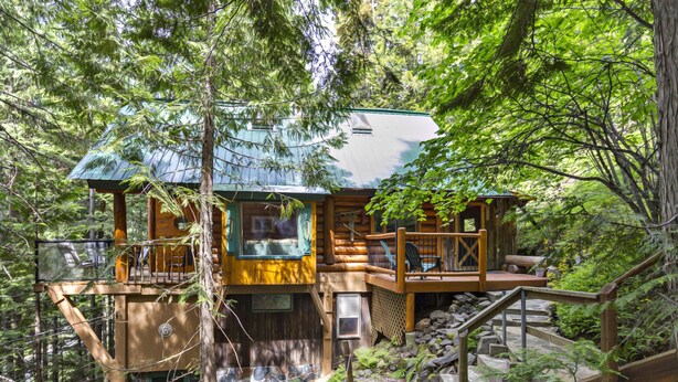 Une cabane en rondins avec des fondations en pierre, une terrasse en bois et un escalier menant à un deuxième étage.
