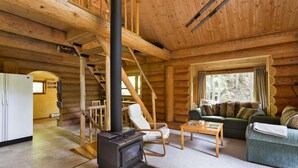L’intérieur d’une cabane en rondins, avec une cheminée, des meubles en bois et un escalier.