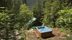 Une cabane en bois, entourée d’une forêt dense, avec un jacuzzi en premier plan.