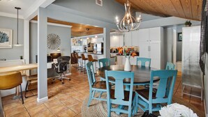 Une cuisine moderne avec un îlot central, un coin repas avec des chaises bleues et un lustre.