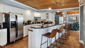 Une cuisine moderne avec des meubles blancs, un réfrigérateur en acier inoxydable, un plafond en bois et un coin bar avec des tabourets.