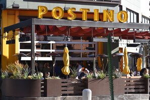 Un restaurant appelé POSTINO, doté d’une terrasse et de parasols jaunes.