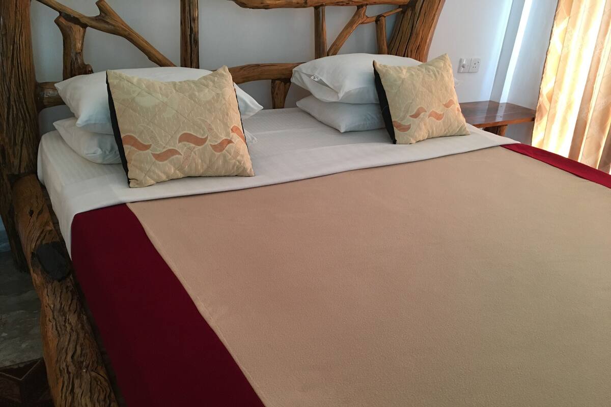 A bed with a wooden headboard, two pillows, and a red blanket.