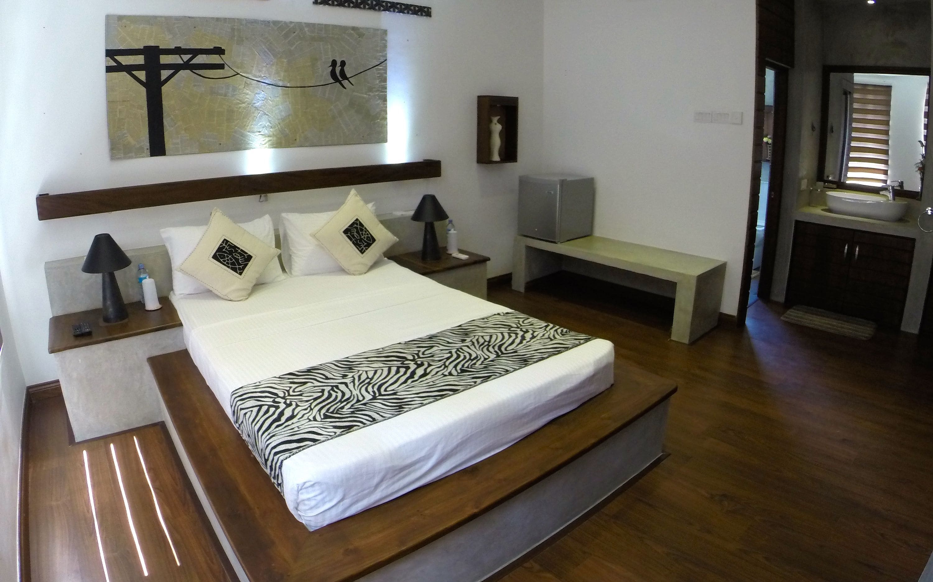 A bedroom with a large bed, bedside tables, a bench, a TV, and a wall art piece.