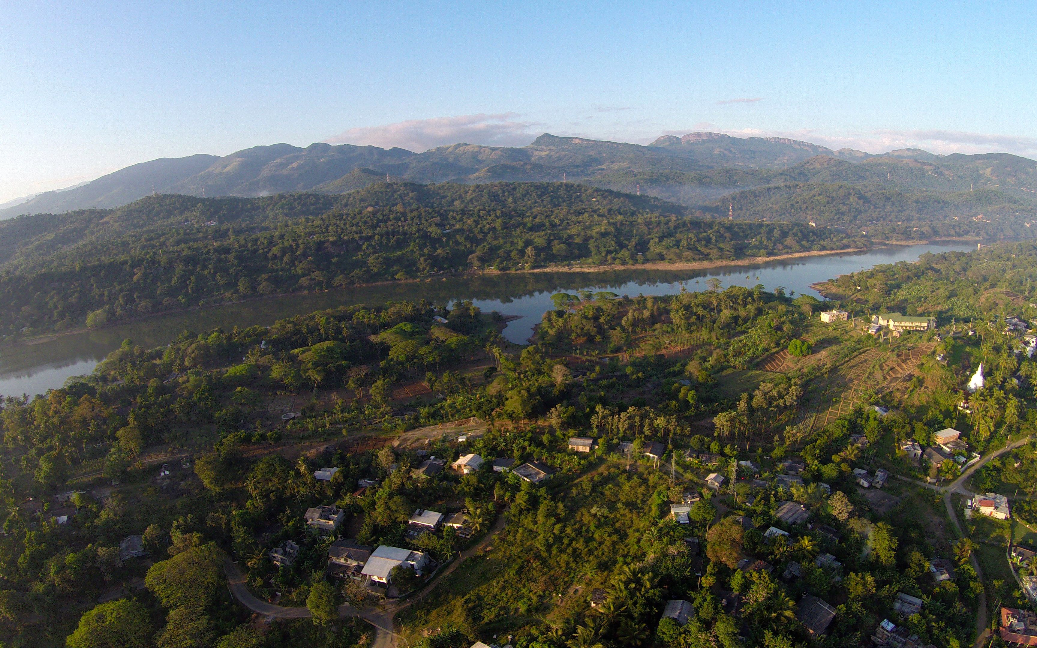 An aerial view of a rural area with scattered houses, a lake, and mountains in the background.