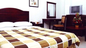 A hotel room with a large bed, a desk with a chair, a television, and a decorative plant.