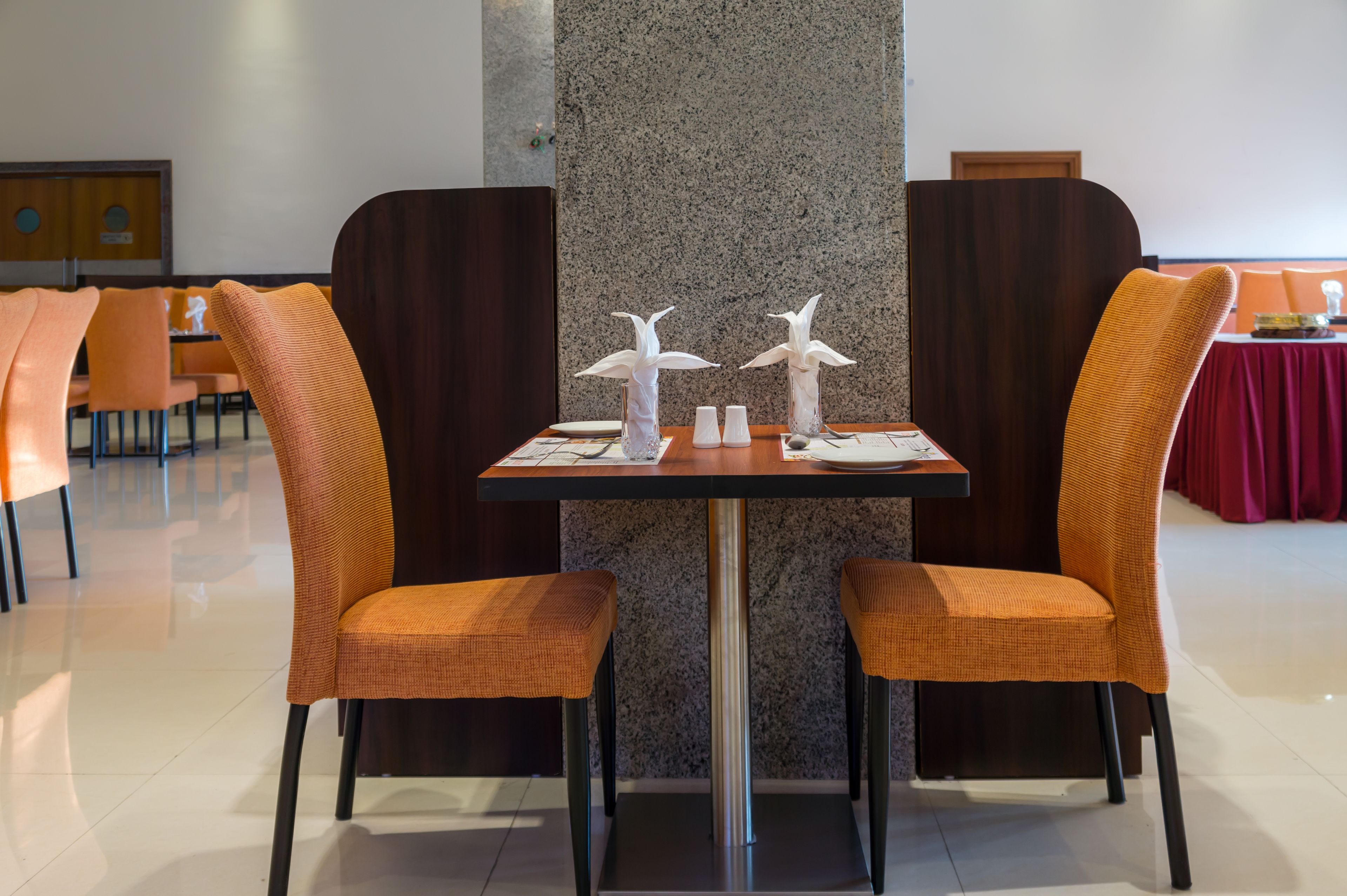 A dining area with a table set for two, featuring orange chairs and a marble pillar.