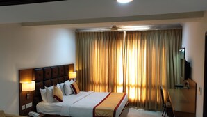 A hotel room with a large bed, two bedside lamps, a flat-screen TV, and a ceiling fan. - Hotel Saptagiri (Hyderabad)
