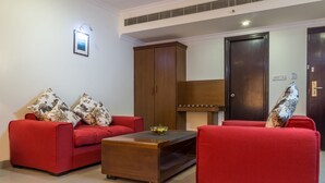 A modern living room with two red sofas, a wooden coffee table, and a large wooden cabinet. - Hotel Saptagiri (Hyderabad)