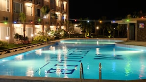 A swimming pool with the words "THE HOTEL" spelled out in the water, surrounded by a building with balconies and string lights. - Mexolie Hotel (Kebumen)