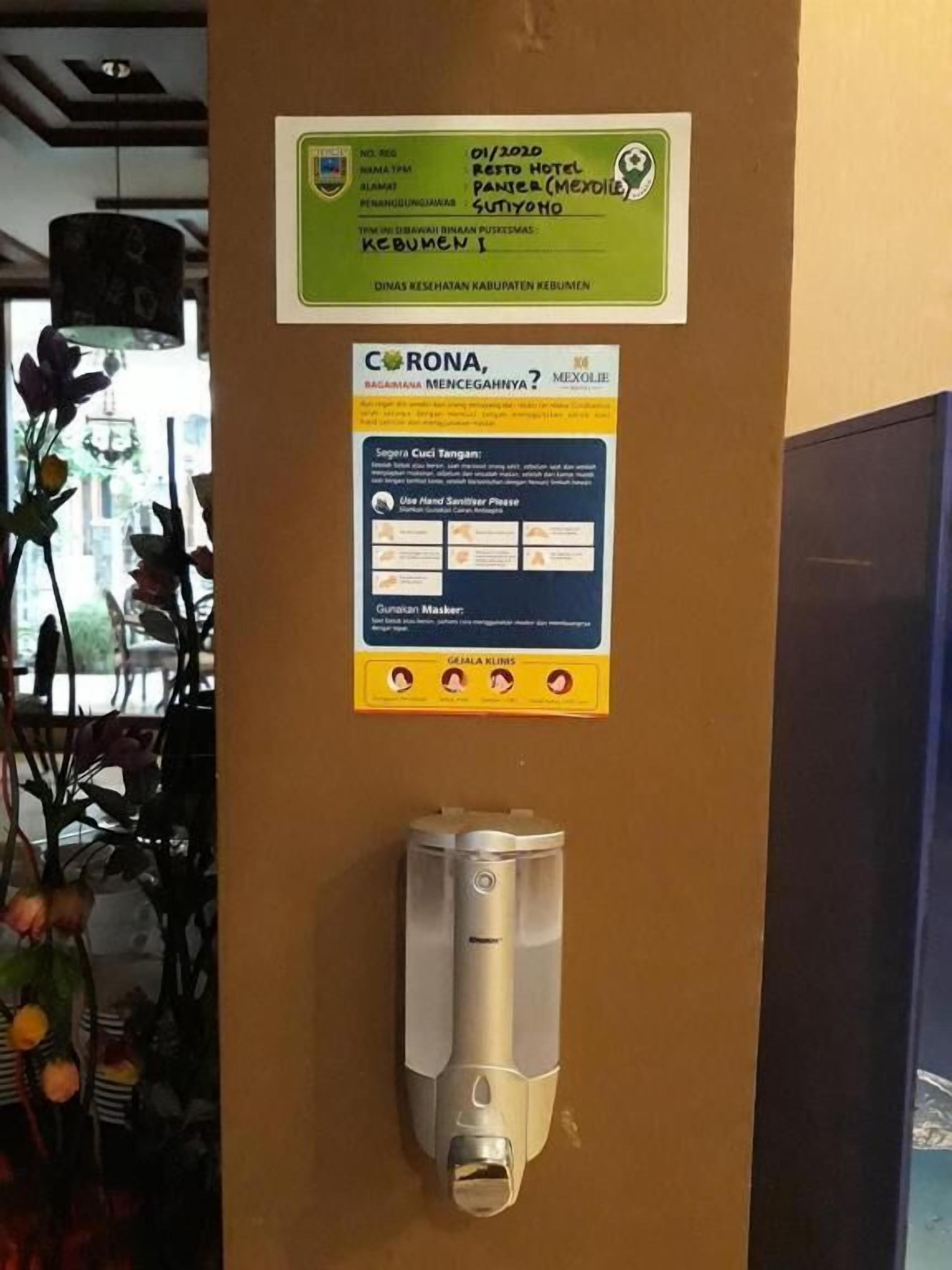 Un mur sur lequel est affiché un panneau indiquant un centre de dépistage de la COVID-19 dans un hôtel, ainsi qu’un distributeur de gel hydroalcoolique et un distributeur de masques.