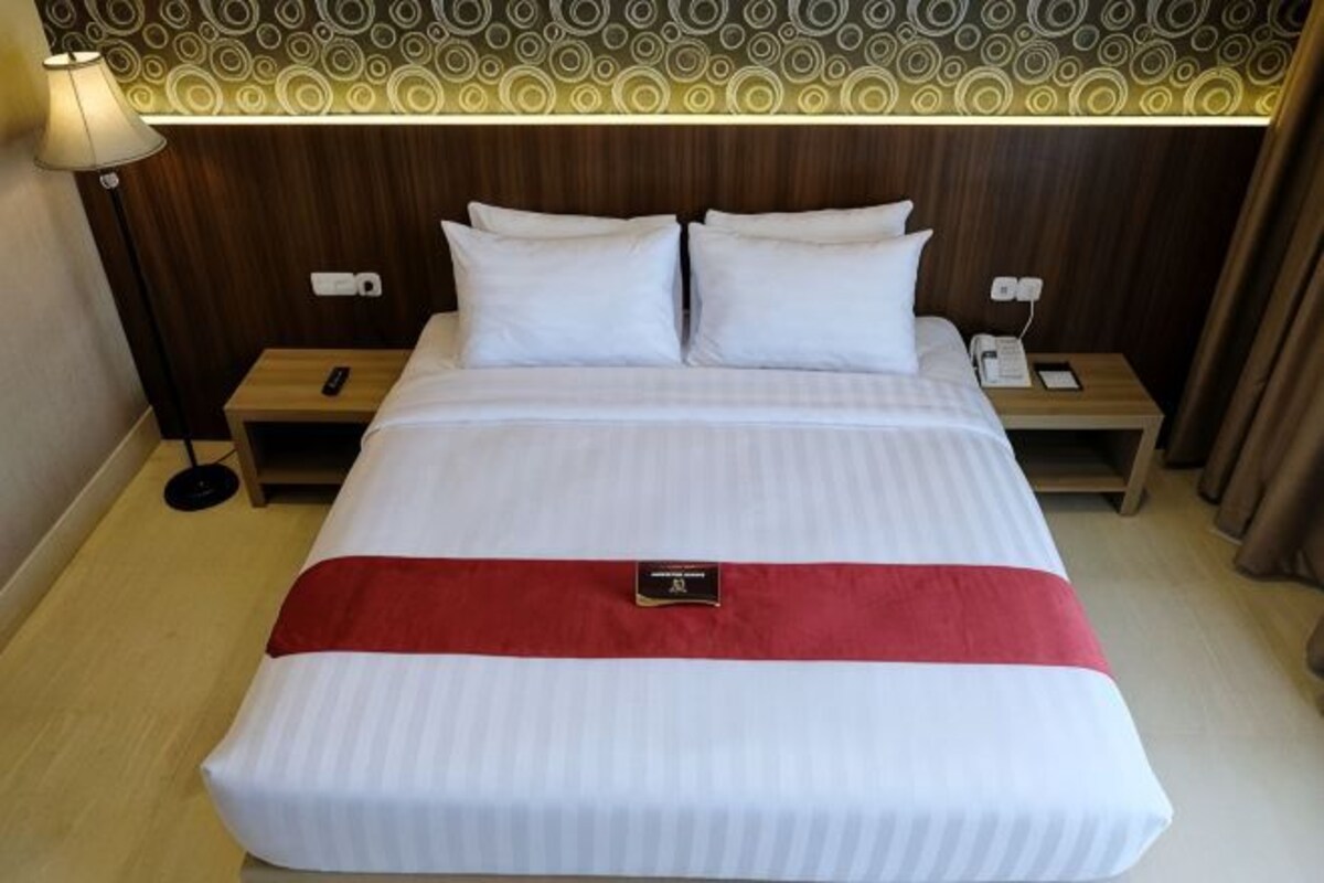 Una habitación de hotel con una cama grande, dos mesitas de noche, una lámpara y un teléfono.