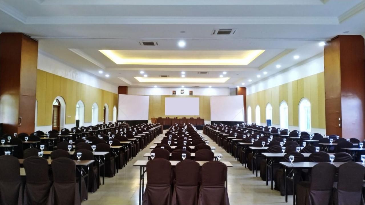 A conference room with rows of tables and chairs, a stage with a screen, and a long aisle.