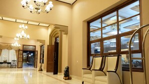 A spacious lobby with a chandelier, a large window with a view, and a seating area with two chairs. - Mexolie Hotel (Kebumen)