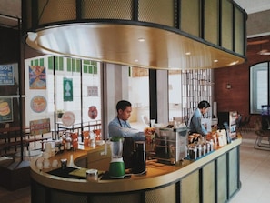 A coffee bar with two baristas, a green blender, and various coffee-making equipment. - Mexolie Hotel (Kebumen)