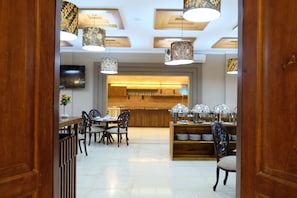 A modern dining area with wooden furniture, pendant lights, and a central kitchen area with a brick backsplash. - Mexolie Hotel (Kebumen)