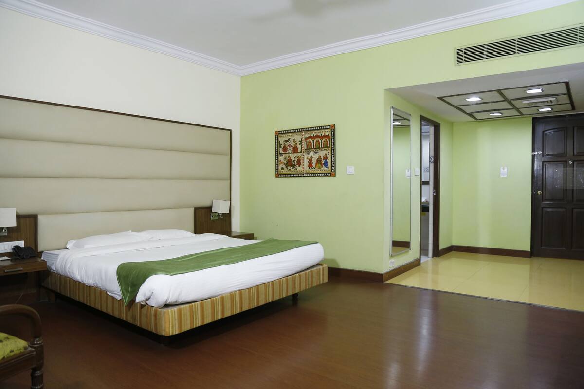 A hotel room with a large bed, a nightstand, a chair, a desk, and a door.