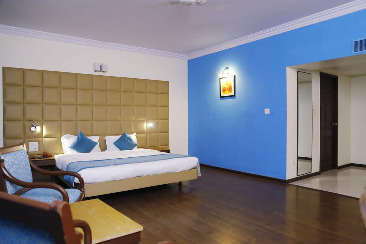 A hotel room with a large bed, a wooden nightstand, a chair, and a blue wall.