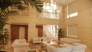 Un'ampia hall, ben illuminata, con soffitto alto, diverse zone relax e una scala che conduce a un piano superiore.