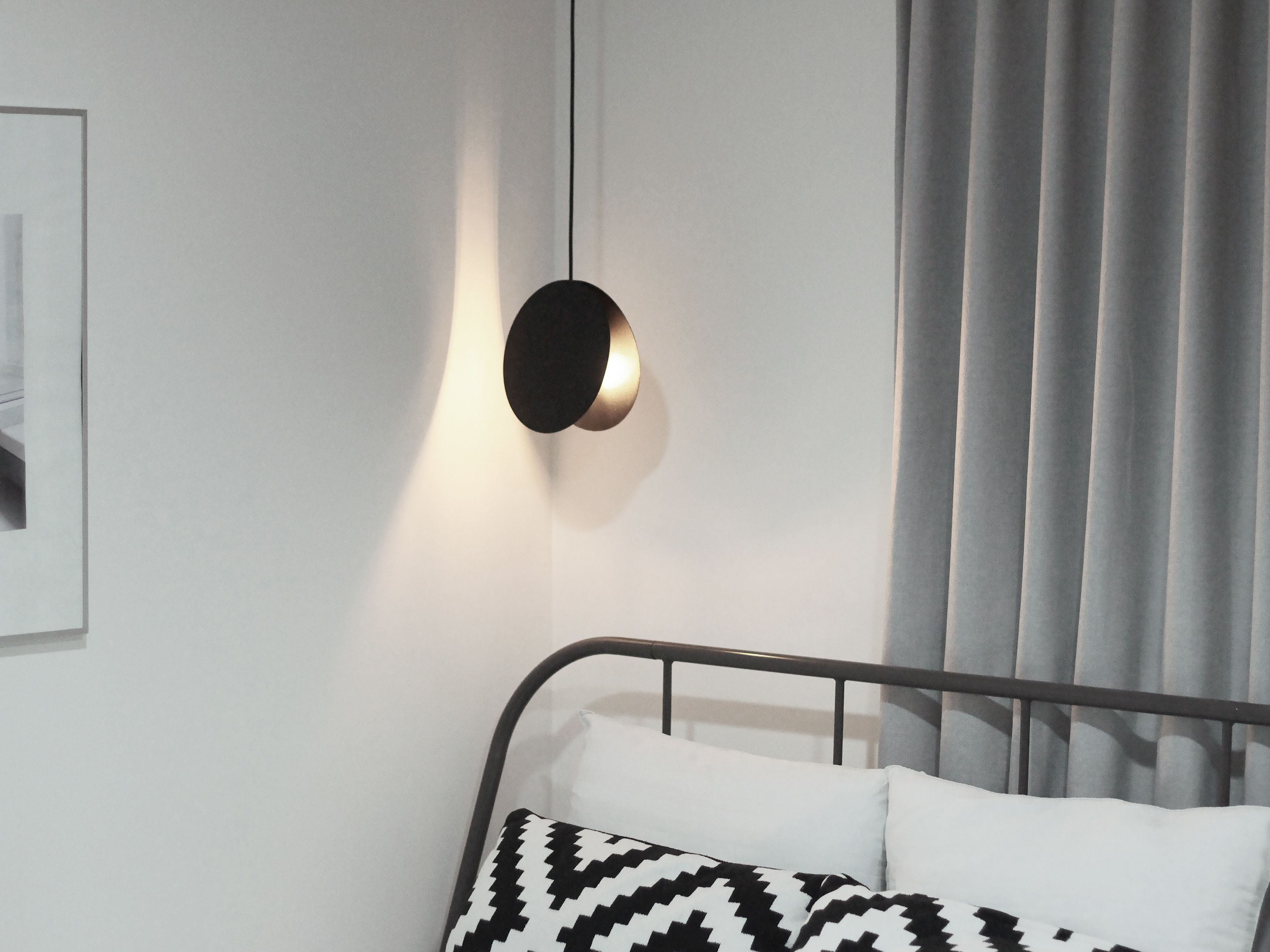 A modern bedroom with a bed, a wall-mounted light fixture, and a window with curtains.
