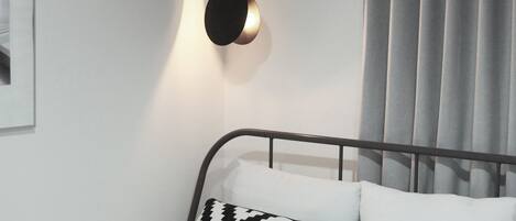 A modern bedroom with a bed, a wall-mounted light fixture, and a window with curtains.