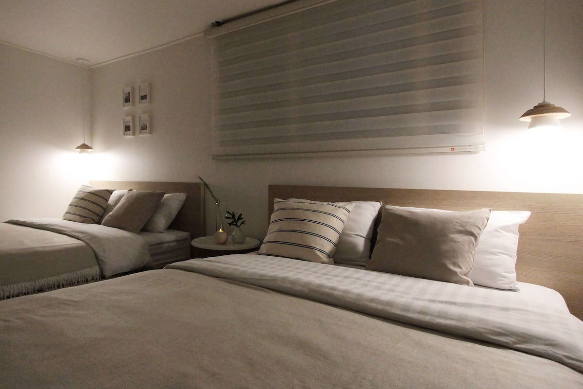 Una habitación de hotel con dos camas, una mesita de noche con lámpara y una ventana con persianas.