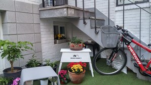 Un pequeño espacio exterior con una planta en maceta, una bicicleta y un letrero que dice "MONO HOUSE 3".