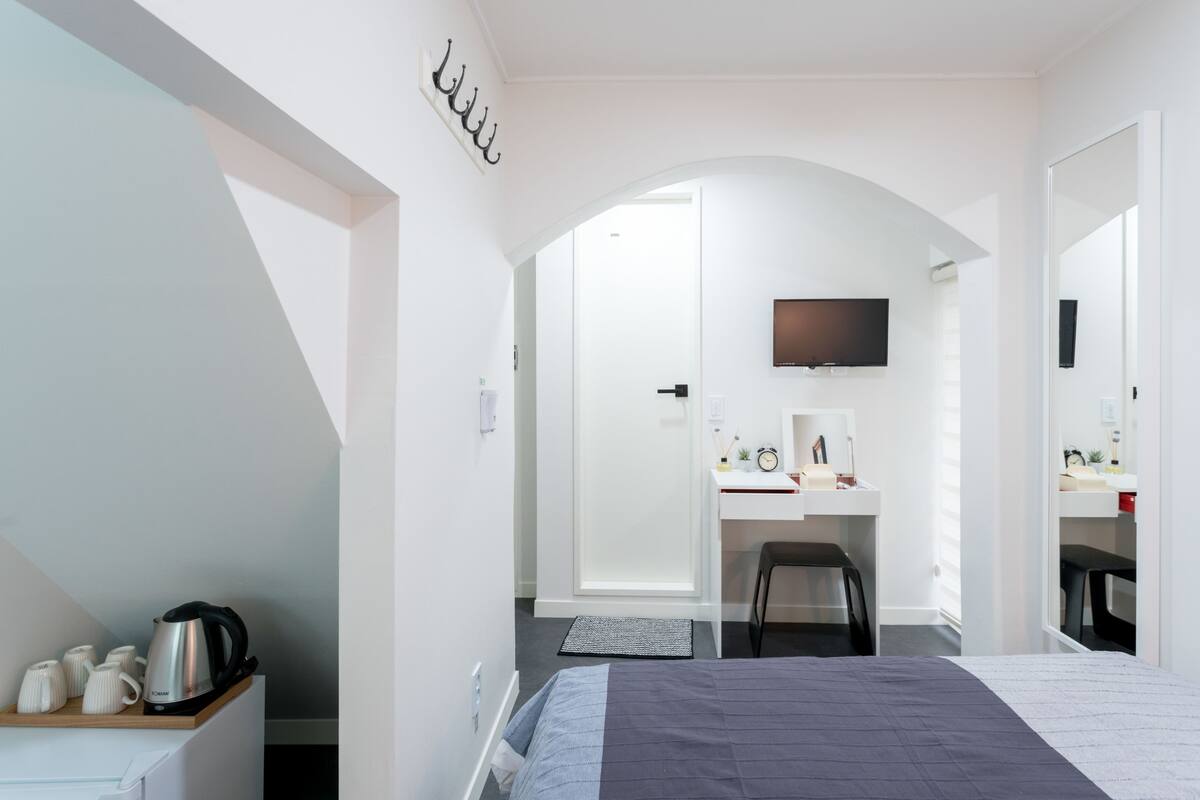 Una habitación de hotel moderna con cama, escritorio con silla, televisor y una pequeña zona de kitchenette.