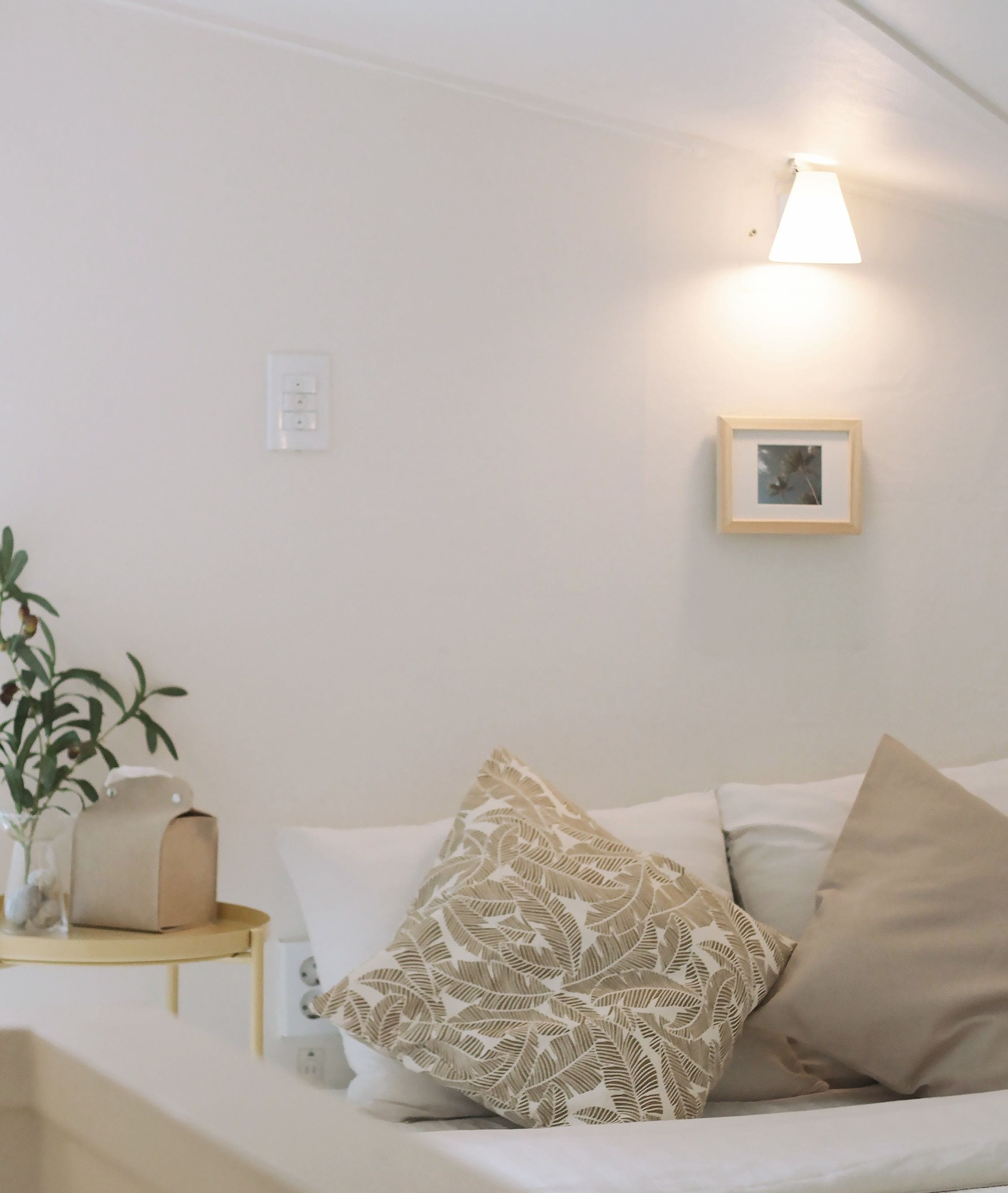 Un salón minimalista con un sofá, una mesita auxiliar, una lámpara de pared y un cuadro enmarcado.
