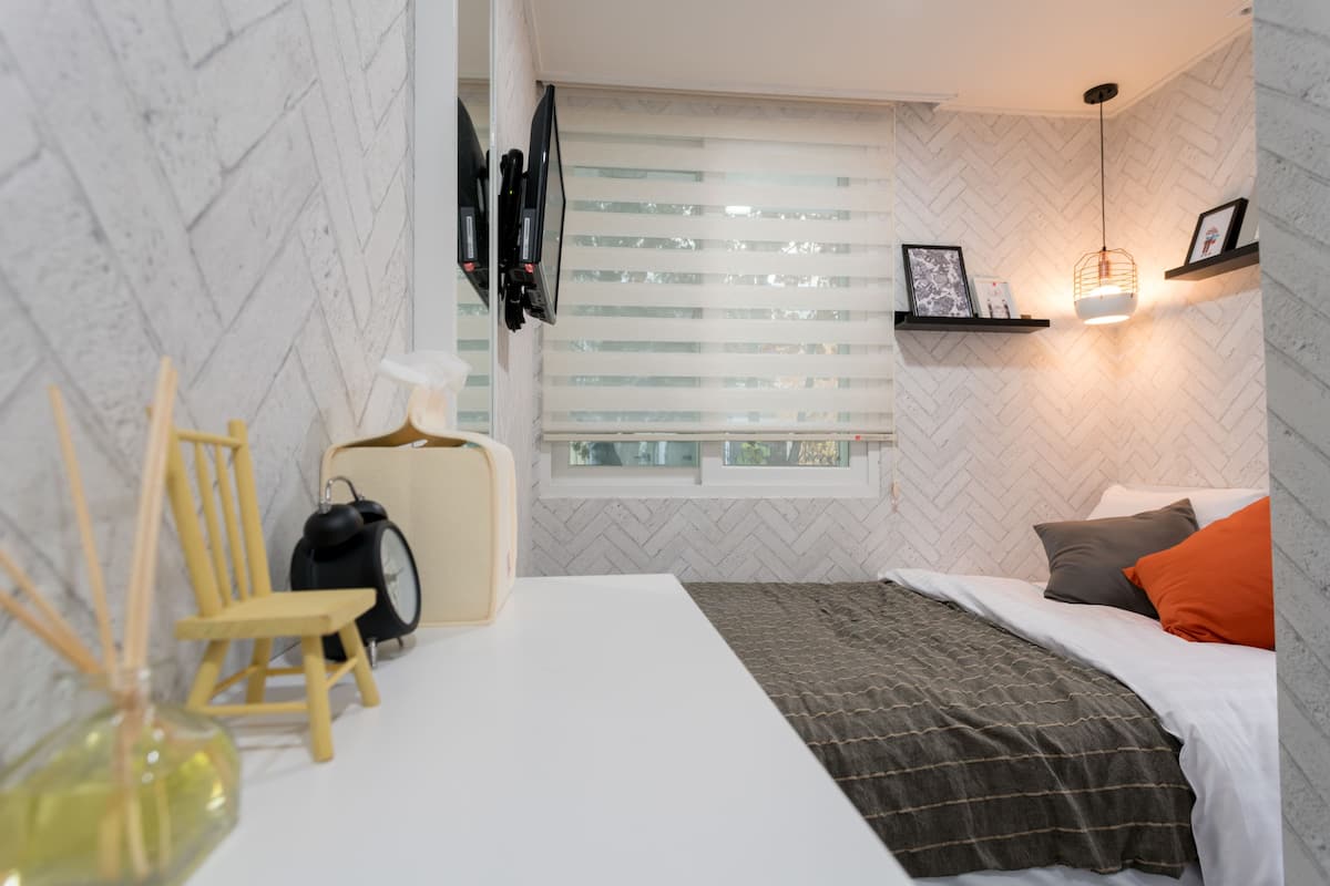 Un dormitorio moderno con una cama blanca, una silla de madera, una mesita y una ventana con persianas.
